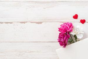 fotografía conceptual del día de las madres de mayo: hermosos claveles y forma de corazón con una tarjeta blanca vacía aislada en una mesa de madera brillante, espacio para copiar, plano, vista superior, maqueta foto