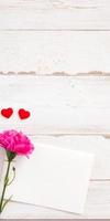 May mothers day concept photography - Beautiful carnations and hearts shape with white empty card isolated on a bright wooden table, copy space, flat lay, top view, mock up photo