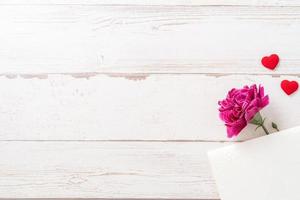 fotografía conceptual del día de las madres de mayo: hermosos claveles y forma de corazón con una tarjeta blanca vacía aislada en una mesa de madera brillante, espacio para copiar, plano, vista superior, maqueta foto