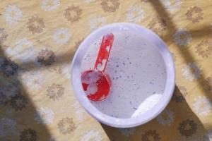 Washing powder in plastic spoon on blue background photo