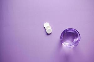 Effervescent soluble tablet pills and glass of water on purple background photo