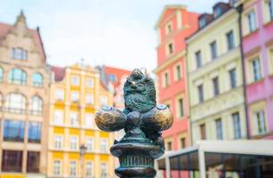 Wroclaw, Poland, May 7, 2019 Dwarf is sitting on street water tap on Rynek Market Square, famous bronze miniature gnome with hat sculpture is a symbol of Wroclaw in old historical city centre photo