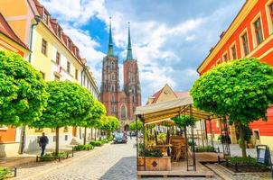 Wroclaw, Poland, May 7, 2019 Street with cobblestone road with green trees, colorful buildings, Cathedral of St. John the Baptist church with two spires in old historical city centre, Ostrow Tumski photo