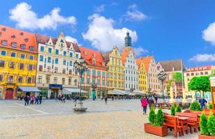 Wroclaw, Poland, May 7, 2019 Row of colorful traditional buildings with art facades, St. Elizabeth Basilica catholic Church and walking people on Rynek Market Square in old historical city centre