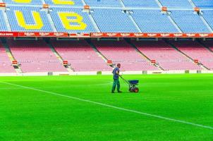 barcelona, españa, 14 de marzo de 2019 el trabajador está sembrando hierba con un esparcidor de fertilizante en el césped del campo verde del camp nou, las tribunas están al fondo. estadio del futbol club barcelona foto
