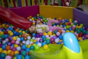 A little girl has fun riding the slides of the sports game complex. Dry Pool with Colored Balls. Children's Sports Exercises.