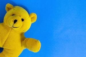 Toy Teddy Bear on Blue. Smiling Yellow Teddy Bear on the Background of the Table, Close-up, Top Down View. photo