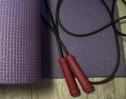 Purple Yoga Mat and Jump Rope with Red Handles on a Light Background. Sports Accessories Lying on a Carpet Closeup. photo