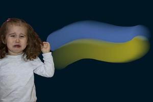 Crying Face of a Girl Looking at the Camera, Cropped Image on the Background of the Flag of Ukraine. Conflict between Russia and Ukraine. Flag of Ukraine and Child. Concept of War. photo