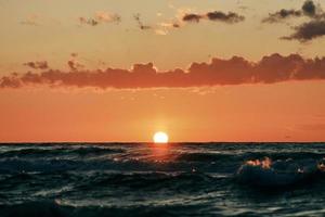 Half sun below horizon over blue sea waves, beautiful sunset over sea, breathtaking seascape photo