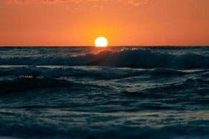 Half sun below horizon over blue sea waves, beautiful sunset over sea, breathtaking seascape photo