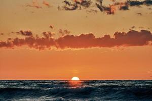 Half sun below horizon over blue sea waves, beautiful sunset over sea, breathtaking seascape photo