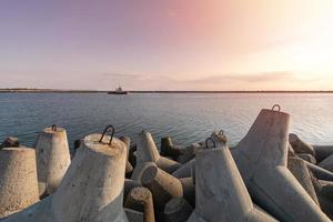 barco-remolcador va en alta mar para remolcar el buque de carga al puerto. hermosa puesta de sol sobre el muelle. rompeolas tetrápodos en el puerto. foto