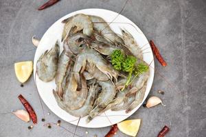 Fresh shrimp prawns for cooking with spices lemon on dark background in the seafood restaurant, raw shrimps on white plate, top view photo