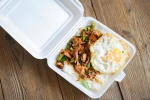 revuelva cerdo frito con pasta de curry rojo y hojas de albahaca con frijol largo y huevo frito en una caja de plástico, comida callejera tailandesa o entrega de comida foto