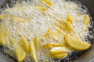 Cooking french fries or fry potatoes in hot oil for potato wedges, Close up fried potatoes in oil on pan photo