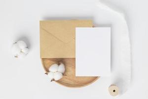 maqueta de invitación de tarjeta de felicitación en blanco en sobre marrón con flor de algodón sobre fondo blanco, composición mínima del lugar de trabajo de la mesa, capa plana, maqueta