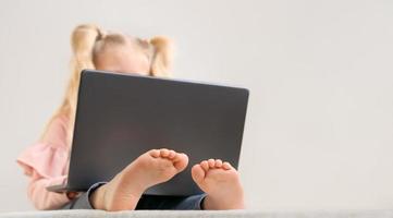 niña pequeña con computadora portátil, solo se ve la parte superior de la cabeza rubia y los pies pequeños