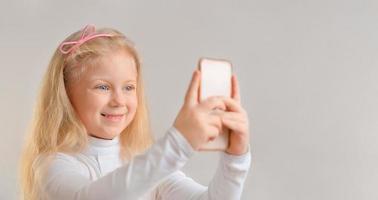 Beautiful smiling little girl taking a selfie photo with smartphone