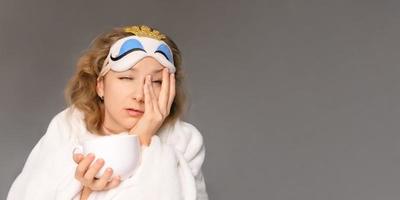 A woman in a sleep mask tries to wake up while drinking coffee photo