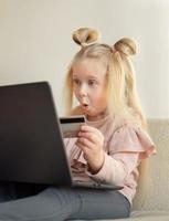 Funny caucasian little girl holding credit card buying online at home photo