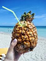 Cocktail in a pineapple in a woman's hand against the backdrop of the sea and sandy beach in Varadero, Cuba photo