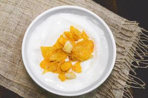 yogur en taza de cerámica tiene copos de maíz sobre fondo de madera. foto