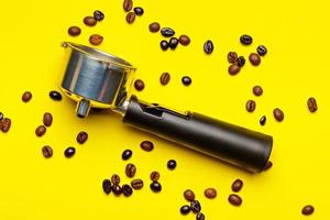 Espresso machine filter holder surrounded by coffee beans on yellow background.