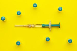 Syringe with several medical vials for injecting on yellow background. Top view. photo