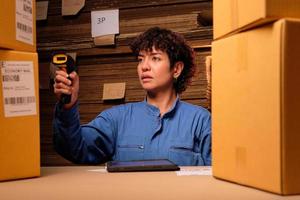 One female worker in safety uniform uses a bar code scanner and tablet to check shipping orders at parcels warehouse, paper manufacture factory for the packing industry, logistic transport service. photo