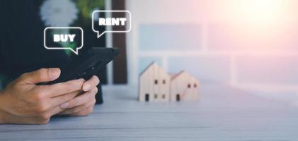 concepto de inversión inmobiliaria. el hombre de negocios usa un teléfono inteligente con una casa emergente para comprar o alquilar. dinero de ahorro, inversión de activos, rendimientos en el futuro y un corredor de vivienda. foto