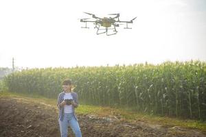 Young smart farmer controlling drone spraying fertilizer and pesticide over farmland,High technology innovations and smart farming photo