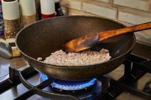 Purple onions are fried in a frying pan on a gas stove. Prepare ingredients and vegetables before cooking photo