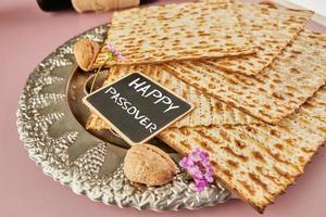 Pesach celebration concept - Jewish holiday Pesach. Matzah on traditional Seder plate with bottle of red wine, nuts on purple background and the inscription Happy Passover photo