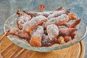 Bugnes, French donuts in transparent plate on wooden board photo