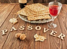 Pesach celebration concept - Jewish holiday Pesach. Matzah on traditional Seder plate with bottle of red wine, glass of wine and nuts on wooden background and the inscription passover photo