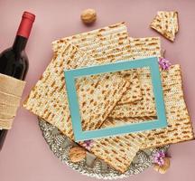 concepto de celebración de pesach - festividad judía pesach. matzá en plato tradicional de seder con botella de vino tinto, nueces sobre fondo morado y marco azul para texto foto