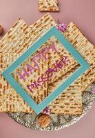 Pesach celebration concept - Jewish holiday Pesach. Matzah on traditional Seder plate with bottle of red wine, nuts on purple background and blue frame with the inscription Happy Passover photo
