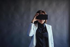 Happy woman on a black background in the studio gets the experience of using VR-glasses virtual reality headset. photo