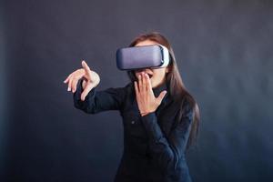 Happy woman on a black background in the studio gets the experience of using VR-glasses virtual reality headset.