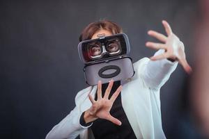 Happy woman on a black background in the studio gets the experience of using VR-glasses virtual reality headset. photo