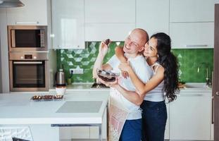 hermosa pareja joven está hablando, mirando a la cámara y sonriendo mientras cocina en la cocina. foto