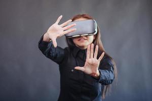 Happy woman on a black background in the studio gets the experience of using VR-glasses virtual reality headset. photo