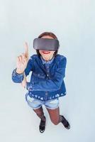 brunette beautiful woman posing in the studio, wearing jeans wear, using VR-glasses virtual reality headsets photo