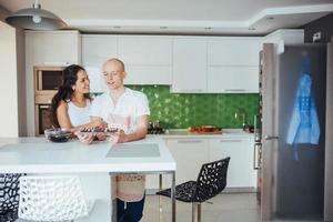 hermosa pareja joven fotografiada sonriendo a la cámara mientras cocina en la cocina en casa. foto