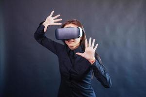 Happy woman on a black background in the studio gets the experience of using VR-glasses virtual reality headset. photo