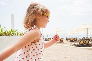 Happy baby girl in a dress on the beach by the sea in summer. photo