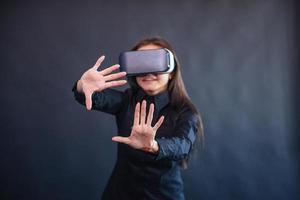 Happy woman on a black background in the studio gets the experience of using VR-glasses virtual reality headset. photo