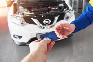Hands of car mechanic with wrench in garage, payment by credit card photo