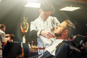 el barbero en el proceso de cortar la barba de las cortadoras eléctricas del cliente en la barbería. foto